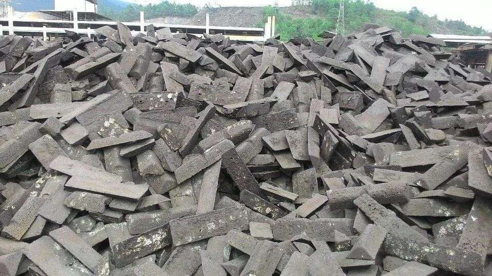 Stacks of dark metal feedstock outdoors beside an industrial building